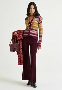 Bunt gestreifte Strickjacke aus Wollmischung mit langen Ärmeln und Knöpfen. Ausgestellte weinrote Hose und ein gemusterter Schal. Handtaschen mit Quaste.