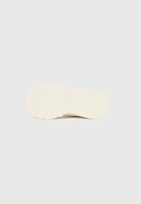 Fehér tornacipő talpa vastag, texturált futófelülettel, mély barázdákkal a tapadás érdekében, és egy húzópánt látható a saroknál.