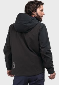 Black outdoor jacket with a hood, featuring a smooth texture, fitted design, and a reflective logo on the back.
