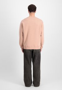 Sudadera rosa claro con un escote redondeado, puños y dobladillo acanalados. Combinada con vaqueros de pierna ancha gris oscuro que tienen bolsillos traseros visibles.