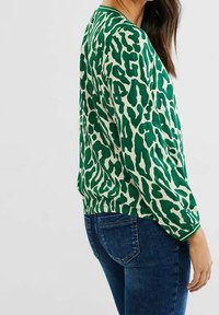 Pullover verde e crema con motivo leopardato, caratterizzato da maniche lunghe e una vestibilità comoda, abbinato a jeans denim blu.