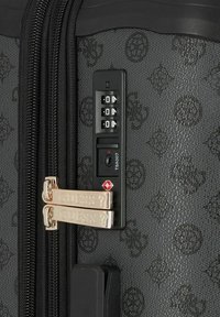 Schwarzer, strukturierten Koffer mit einem Kombinationsschloss, goldfarbenen Reißverschlüssen mit eingraviertem "GUESS" und einem TSA-zugelassenen Schloss-Symbol.