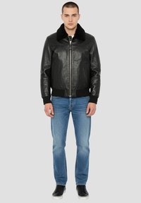 Giacca bomber nera in pelle con colletto in pelliccia sintetica, zip sul davanti, polsini e orlo a coste, abbinata a jeans azzurri e sneakers nere.