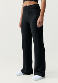 Svarta sportbyxor med en bred, ribbad midja. Har en subtil struktur och raka ben, i kombination med vita skor.