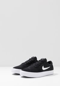 Černé semišové tenisky s bílými gumovými podrážkami a tkaničkami, na boku s bílým logem Nike a značkováním na jazyku.