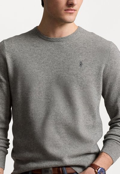 Grå strikket sweater med rund hals og lange ærmer. Har et lille broderet logo på brystet. Blød tekstur og tætsiddende design.