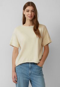Crème-kleurig t-shirt met korte mouwen, een ronde halslijn, een zachte textuur, een ontspannen pasvorm en opgerolde mouwen, gecombineerd met lichtblauwe jeans.