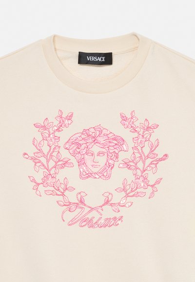 Kremfarvet sweatshirt med lyserød broderet Medusa-hoved, blomstergrene og teksten "Versace" under designet.