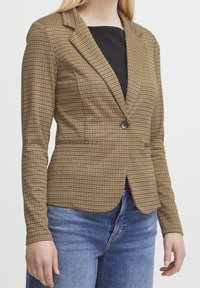 Veste à carreaux marron et beige, dotée d'une fermeture à un bouton, d'un col à revers crantés et de manches longues. Le tissu présente une texture lisse.