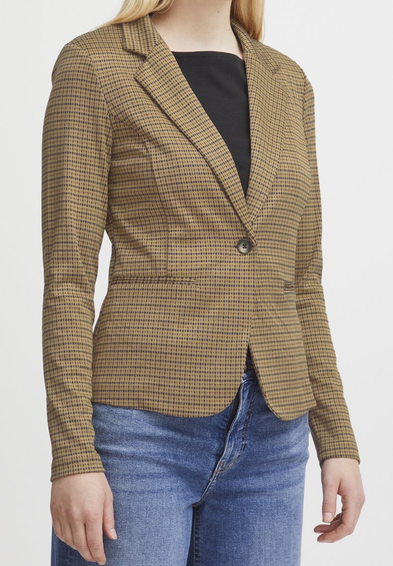 Veste à carreaux marron et beige, dotée d'une fermeture à un bouton, d'un col à revers crantés et de manches longues. Le tissu présente une texture lisse.
