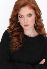 Maglione nero lavorato a maglia con scollo tondo, caratterizzato da una texture morbida. Indossato da una persona con capelli rossi mossi e un trucco leggero.