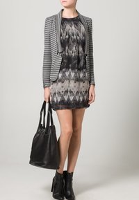 Blazer a rayas, vestido negro y gris con estampado, bolsa de cuero negra y botas de tobillo. Texturas suaves y diseño ajustado.