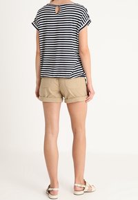Camiseta a rayas azul marino y blanca con un escote en forma de lágrima en la parte posterior, combinada con pantalones cortos beige enrollados y sandalias claras. Ajuste casual y tela suave.