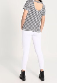 Top de rayas blanco y negro de manga corta con diseño de espalda descubierta, combinado con jeans ajustados blancos y botines negros.