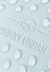 Superficie testurizzata blu chiaro con il logo in rilievo "JOHNNY URBAN", caratterizzato da gocce arrotondate che assomigliano a gocce d'acqua e dettagli circolari.
