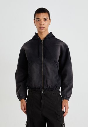 Veste bomber noire à capuche fabriquée en tissu robuste, avec une fermeture éclair à l'avant, des poignets élastiques et une taille élastique. Comprend deux poches latérales.