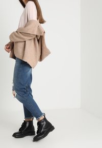 Sorte snørebåndsstøvler, lyserød og beige oversized sweater, slidte blå jeans med frynset kant. Glat tekstur og afslappet pasform.