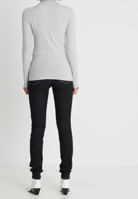 Graues Langarmshirt mit hohem Kragen, kombiniert mit dunklen Skinny Jeans. Weiße Absatzstiefel und ein schlichtes Design, ohne sichtbare Muster oder Akzente.