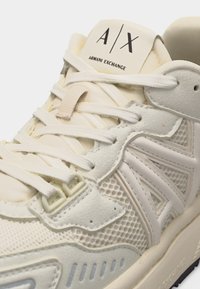 Gros plan sur une basket blanche Armani Exchange avec des panneaux texturés, des lacets blancs et le logo A|X sur la languette.