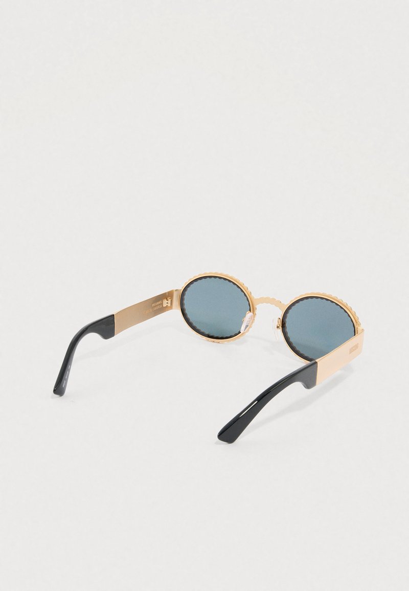 Ronde zonnebril met gegolfde gouden montuur en donkergroene glazen. Voorzien van zwarte pootjes en een logo detail op de zijkant van het montuur.