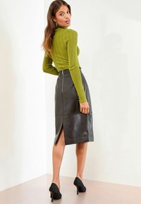 Žalių raištinių megztinių ir juodų odinių pieštukinių sijonų su šoniniu įpjovimu. Suknelė derinama su juodais aukštakulniais batais.