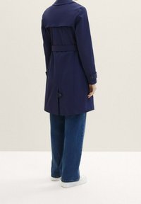 Námořnický trenčkot s páskem v pase, knoflíkovými manžetami a zadním rozparkem. Hladká látka s jemnými svislými pruhy. Džíny s širokými nohavicemi.