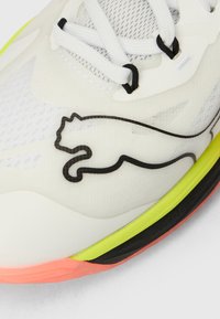 Άσπρο αθλητικό παπούτσι με επάνω μέρος από δίχτυ και συνθετικό υλικό. Διαθέτει μαύρο λογότυπο Puma, έντονες πράσινες και ροζ λεπτομέρειες, και υφασμένο πέλμα.