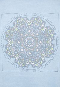 Ljusblå t-shirt med en detaljerad, flerfärgad mandala-design i mitten med en cirkulär textkant som säger "Vår vänlighet och medkänsla."