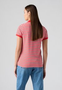 Polo rouge et blanc à rayures avec manches courtes et col côtelé, associé à un jean en denim bleu clair. Design simple et coupe décontractée.