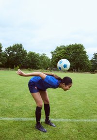 Blue athletic jersey and shorts with a patterned design, knee-high black socks, and black soccer cleats; a soccer ball hovers above the head.