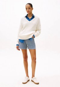 Valge soonikkoega kampsun, sinine nööbitav särk, triibulised lühikesed püksid ja valged jalanõud pruunide talladega. Lihtne ja vabaaja riietus kihilistest materjalidest.