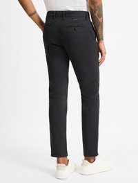 Dunkelgraue Hose aus strukturiertem Stoff, mit figurschnitt und Gesäßtaschen mit Knopfverschluss, kombiniert mit weißen Sneakers.