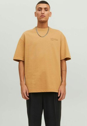 Beige oversized t-shirt lavet af blød bomuld, med korte ærmer og rund halsudskæring, prydet med et minimalistisk tekstdesign på forsiden.