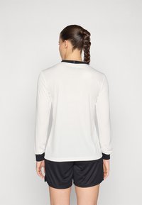 Long-sleeve white athletic top with ribbed texture and black accents at the collar and cuffs, paired with black shorts.