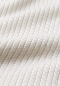 Tissu blanc à côtes avec des lignes verticales, texture douce et surface légèrement en relief. Le matériau semble épais et souple.