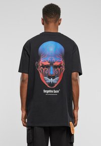 Black t-shirt featuring a colorful graphic of a stylized face and moth on the back, with a brand label on the side seam.