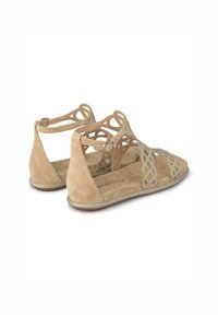Sandali in suede beige con design a intagliature intricate, arricchiti con accenti metallici. Suole piatte con una texture morbida e cinturini alla caviglia.