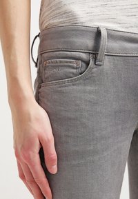 Vaqueros de denim gris con un diseño ajustado, que cuentan con un pequeño bolsillo frontal, costuras sutiles y una textura suave. La cintura incluye un pasador para cinturón.
