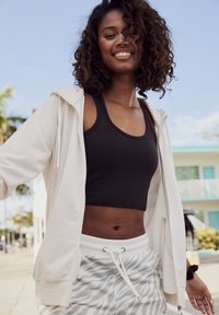 Lässiges Outfit mit einem hellbeigen Reißverschluss-Hoodie, einem schwarzen Crop-Top und grauen gestreiften Shorts mit einem Kordelzug.