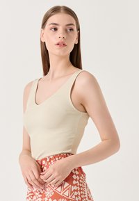 Débardeur beige à côtes avec un col en V et de larges bretelles, porté avec une jupe orange à motifs présentant des designs géométriques.
