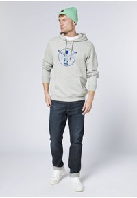 Light gray hoodie with blue graphic print, kangaroo pocket; paired with dark denim jeans and white sneakers. Mint green beanie on head.