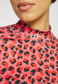 Red and black leopard print high-collar top made from stretchy material, featuring visible stitching and a logo on the neckline.