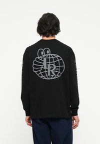 Černé triko s dlouhým rukávem, na zadní straně s velkým šedým grafickým motivem zeměkoule a rukou, s textem na rukávech. Bavlněný materiál, pohodlný střih.