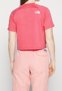 Krátký rukáv, zkrácený tričko z lehké, texturované růžové látky s vyztuženými švy. Logo tištěné bílou barvou na horní části zad.