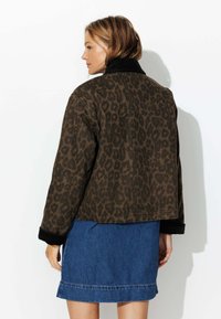 Veste à imprimé léopard en tissu brun foncé et noir, avec un col côtelé et une coupe courte, portée sur une jupe en jean.