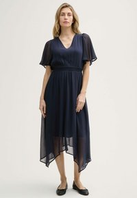 Navyblaues Kleid mit transparenten kurzen Ärmeln, V-Ausschnitt, elastischem Bund und asymmetrischem Saum. Der Stoff wirkt leicht und fließend.