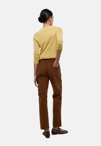 Pull en laine jaune, pantalon en velours côtelé marron et chaussures tissées marron. Le pull a un col rond et des manches ajustées, les pantalons ont des poches arrière.
