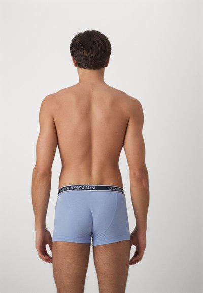 Svetlomodré bavlnené boxerky s čiernym elastickým pásom, na ktorom je logo "Emporio Armani", zobrazené zozadu.