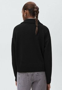 Čierny pletený kardigán s voľným strihom, s rebrovaným lemom a golierom. V kombinácii so šedými džínsy s vysokým pásom v jemnej textúre.