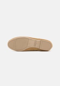 Pantofi din suede de culoare bej, cu o talpă din cauciuc flexibilă. Talpa exterioară are un model texturat pentru aderență și detalii subtile de branding.